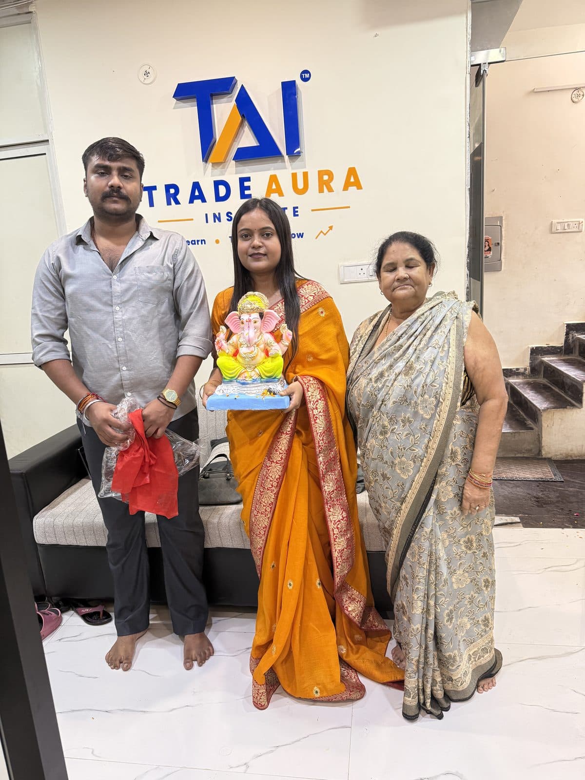 TradeAura team members holding a Ganesh idol in front of the TradeAura Institute logo