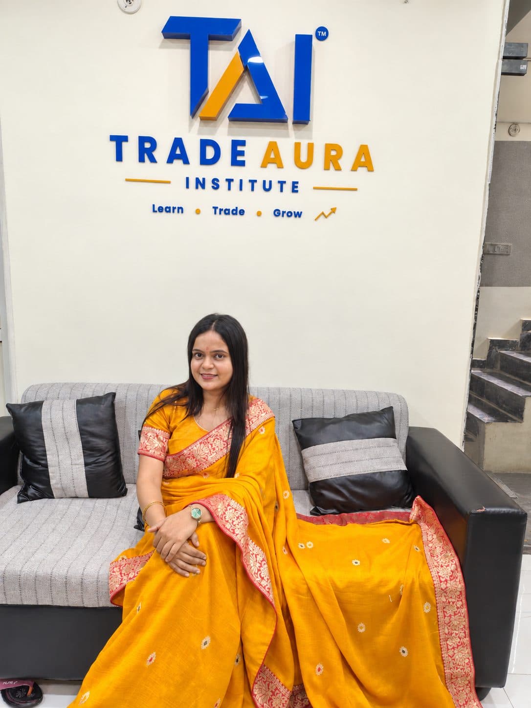 TradeAura team member in a yellow saree seated beneath the TradeAura Institute logo