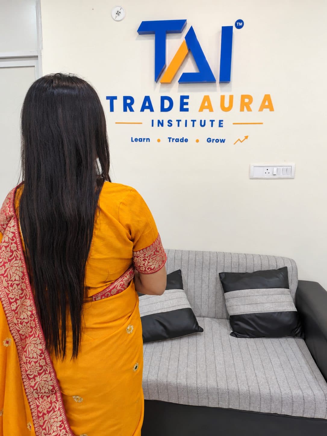 TradeAura team member in a traditional saree facing the TradeAura Institute logo