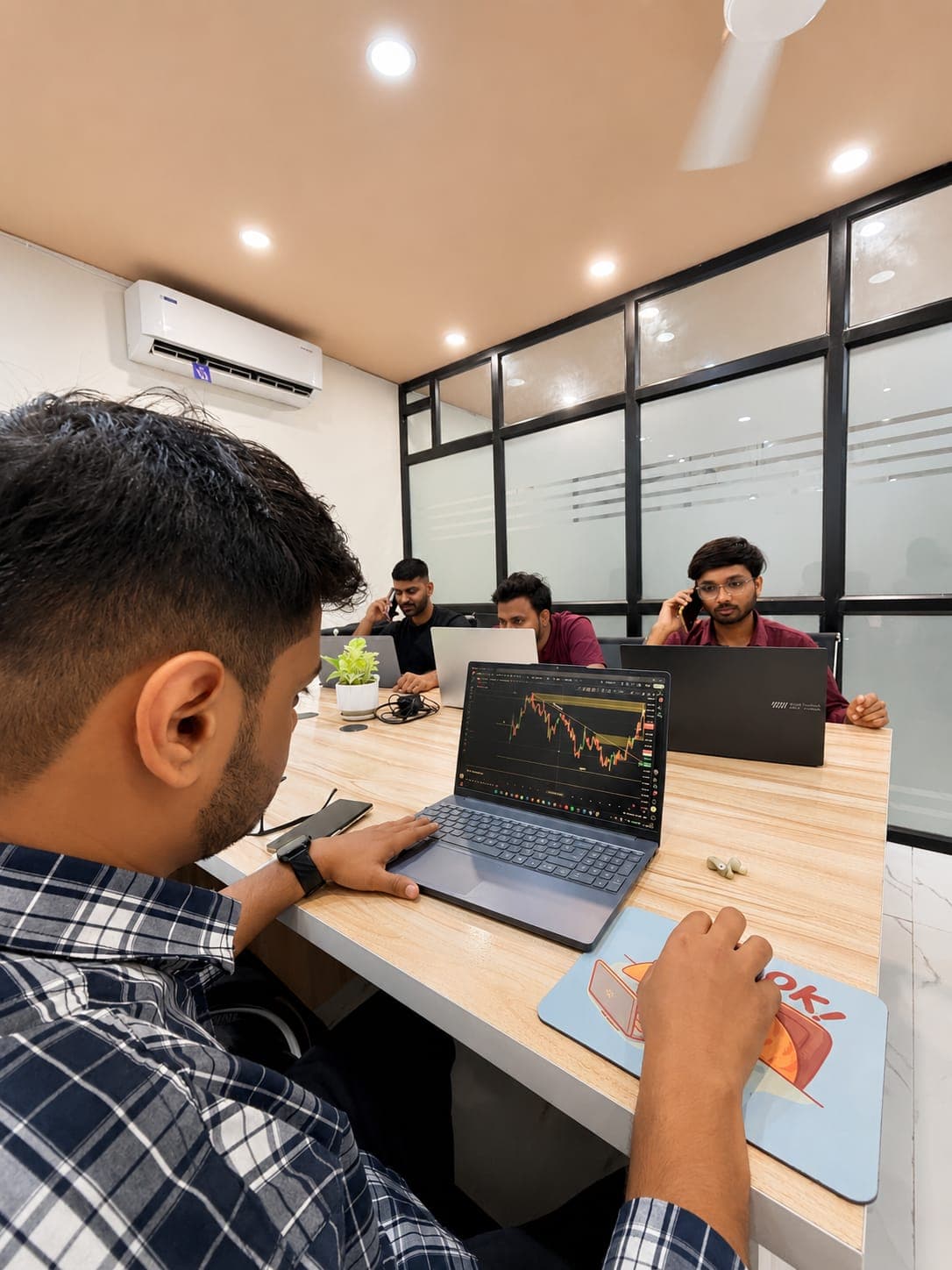 A TradeAura student reviewing a live price chart while classmates take calls in the trading room