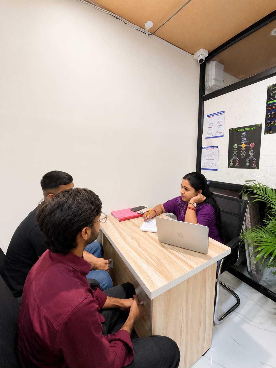 TradeAura mentor explaining a trading strategy to students beside classic chart-pattern posters